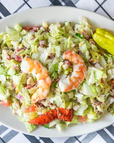 Garbage_Salad-1 A white bowl of chopped salad topped with two large shrimp, a roasted red pepper, and a pepperoncini.