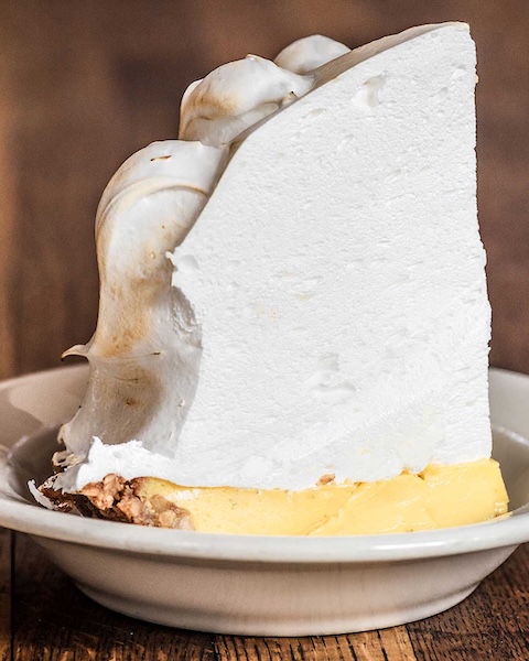 Key-Lime-Pie Slice of lemon Key pie with thick toasted topping on a white plate against a wooden background.